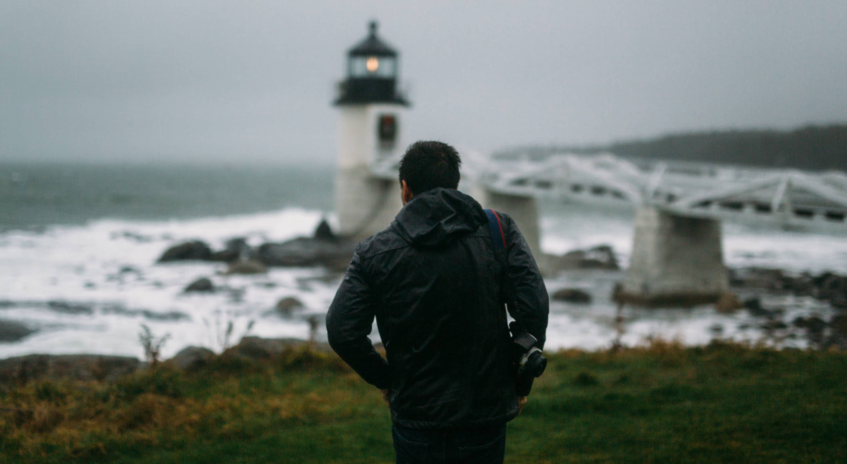 Man with a camera walking towards a lighthouse in Maine