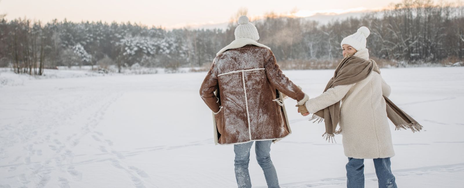 A couple dressed in winter clothes are outside holding hands surrounded by snow.