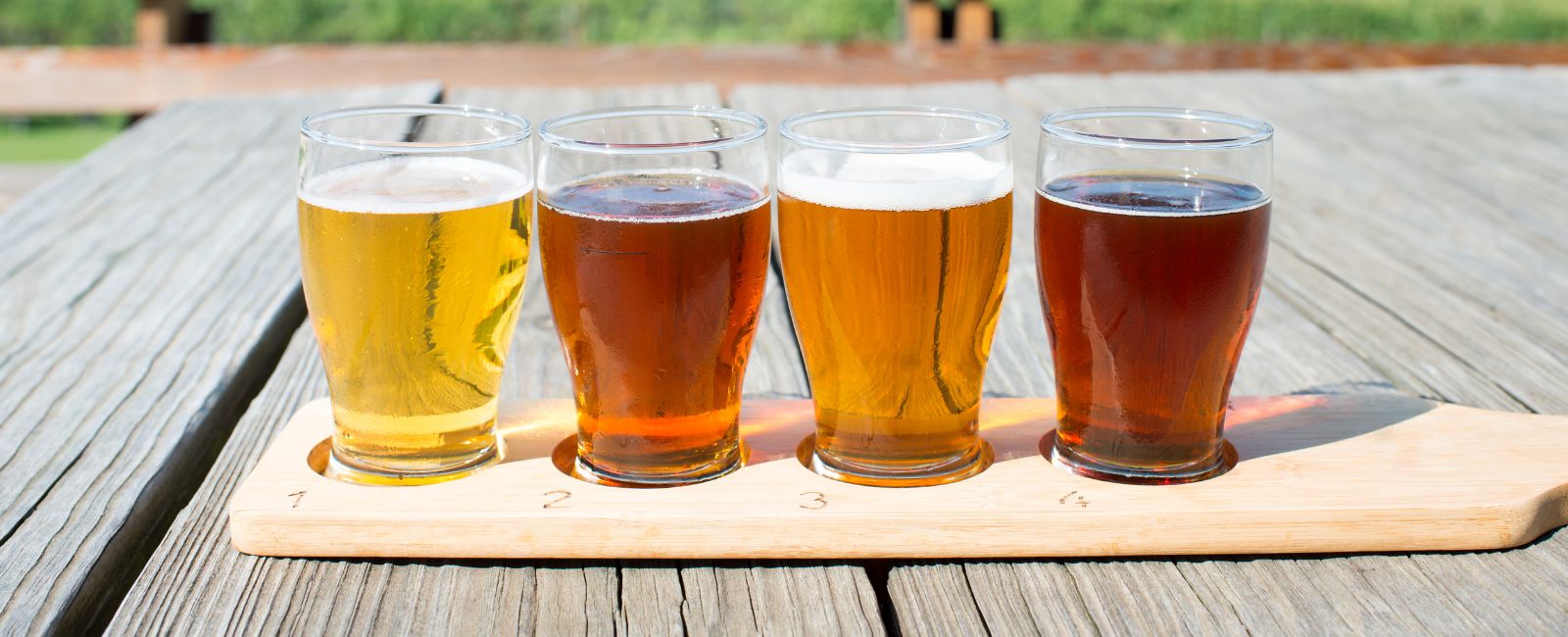 flight of four beer flavors on a wooden table outside