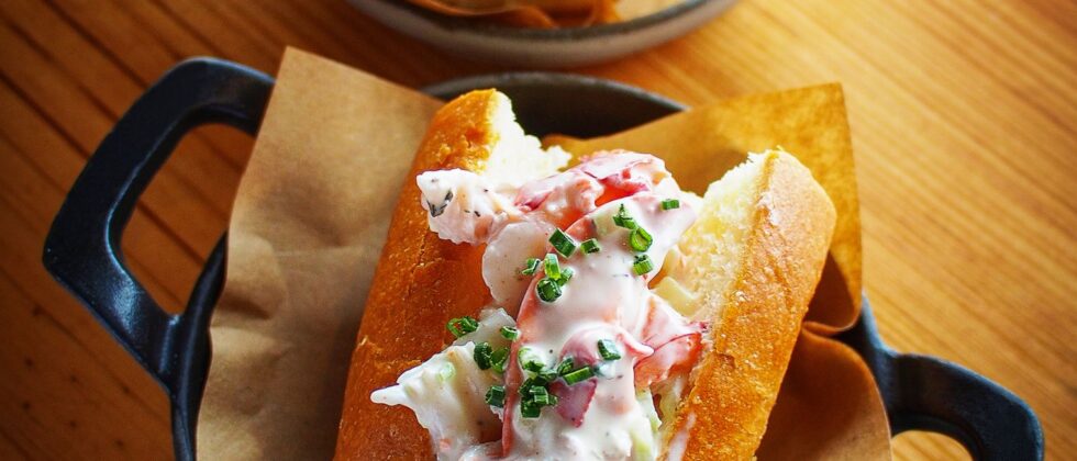 A close-up of a mini lobster roll with fresh, chopped chives in a pan sitting on a wooden table