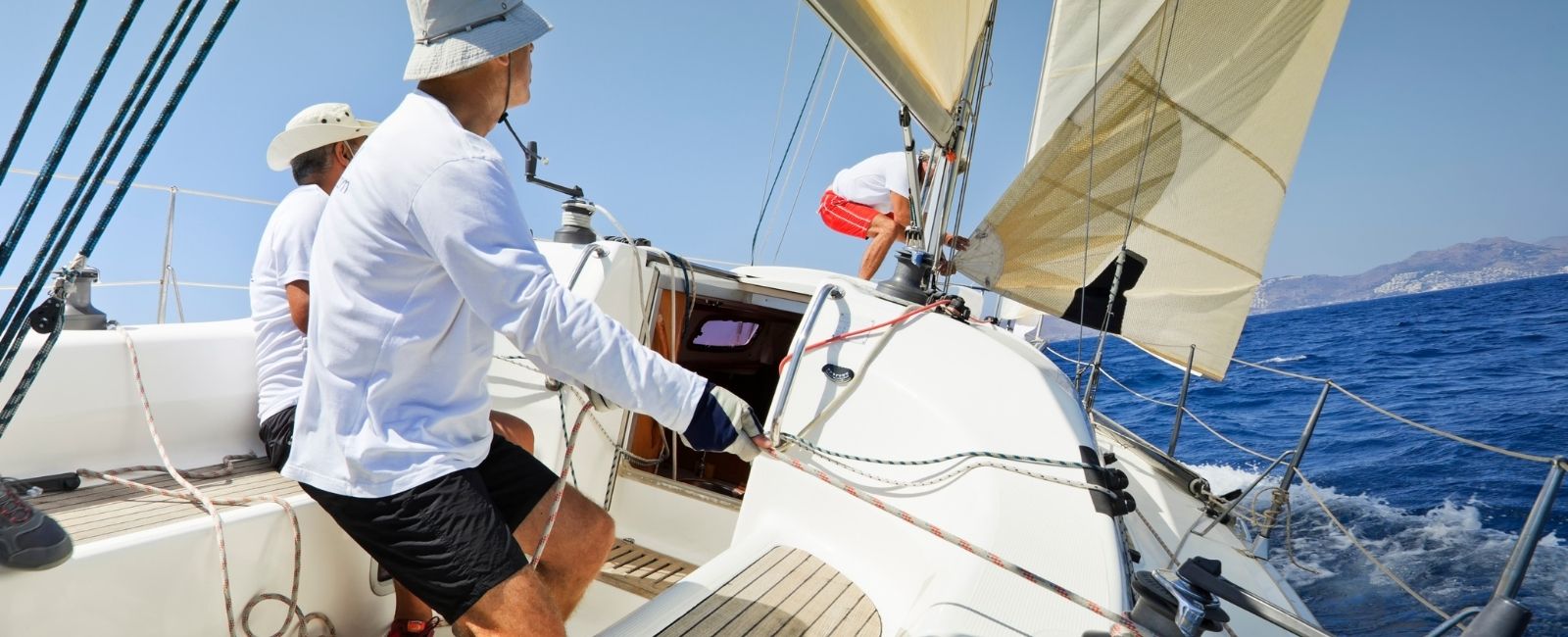 three men in white shirts and sun hats sailing a white sailboat on the blue ocean waters